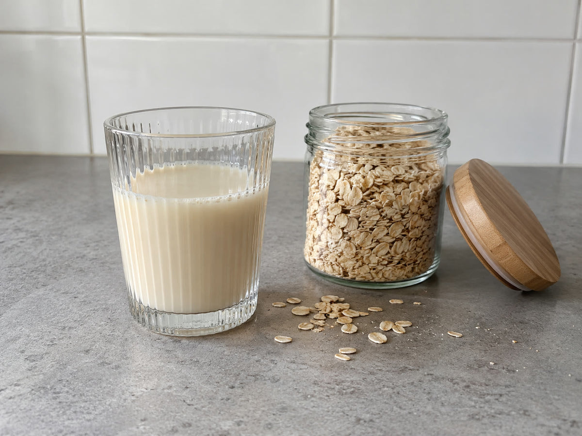 Een glas zelfgemaakte havermelk op het aanrecht, naast een pot havermout