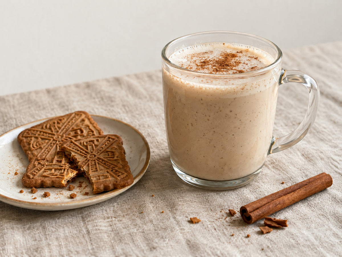 Een mok speculaasmelk naast een bordje speculaasjes en een kaneelstokje